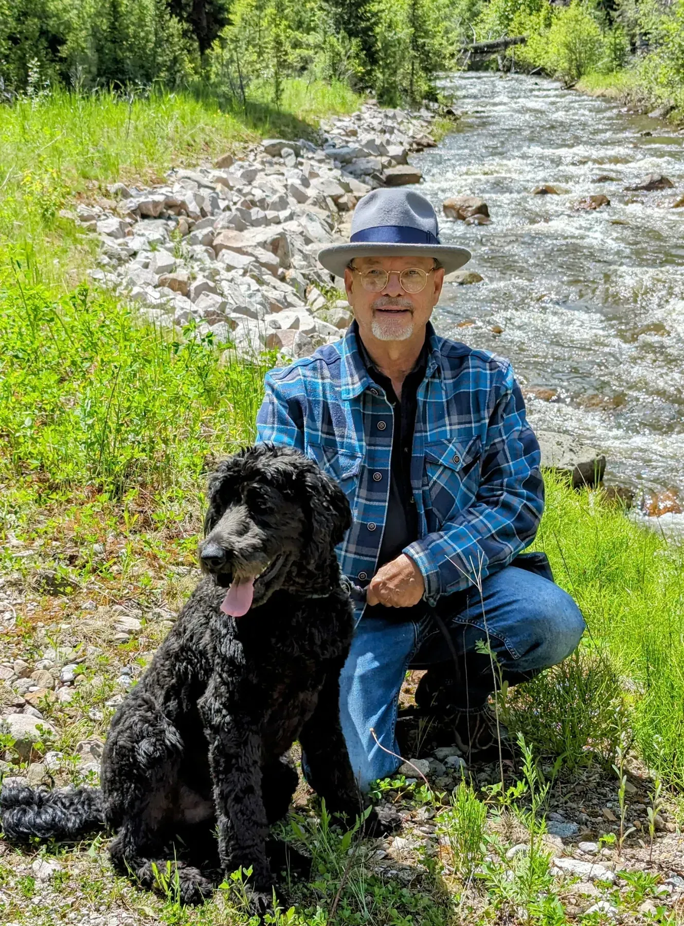 Michael J. Kalous kneeling beside his dog, Tobias, near a Montana mountain stream